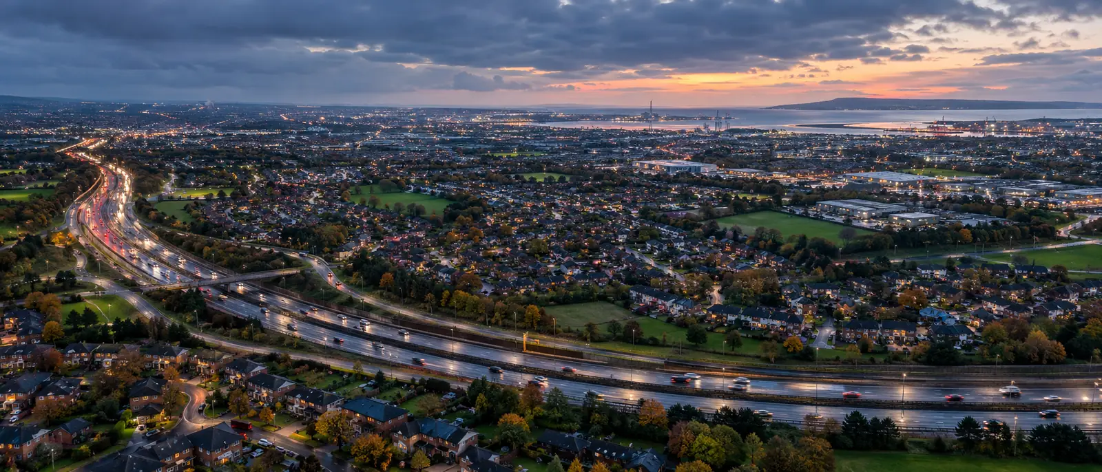 Dublin at dusk from the air, the M50 curving through the suburbs and Dublin Bay behind