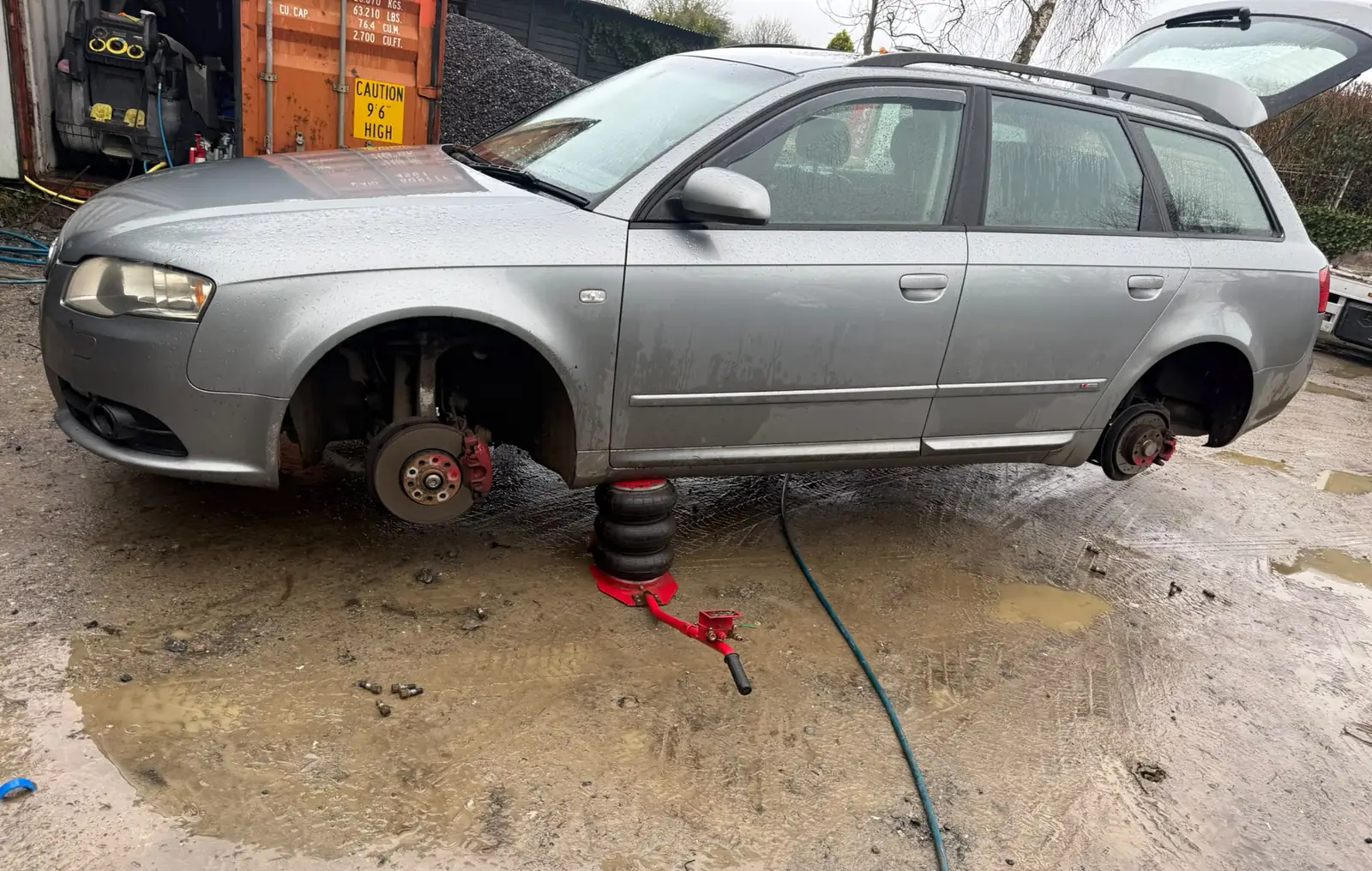 Estate car on an air jack with the wheels off, being repaired on site by a mobile mechanic