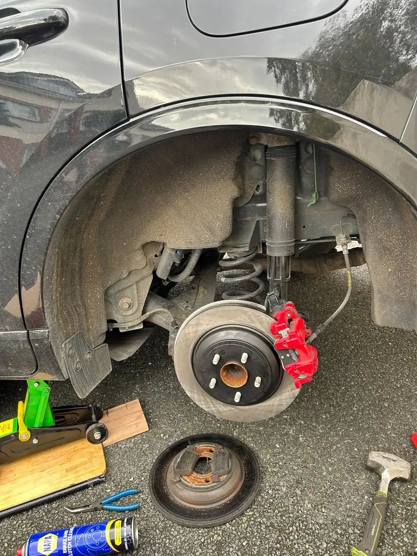 Rear wheel arch with the new brake disc and caliper fitted, jack and tools on the driveway