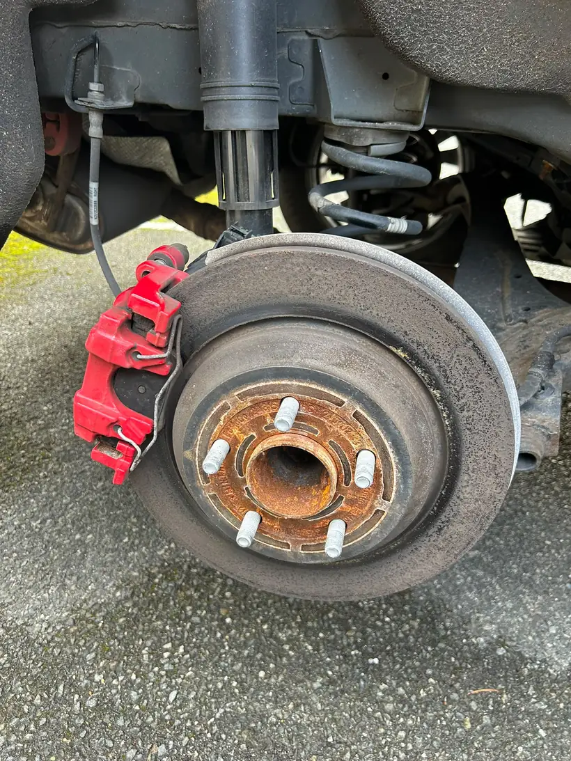Worn, rusted rear brake disc before replacement, red caliper still in place