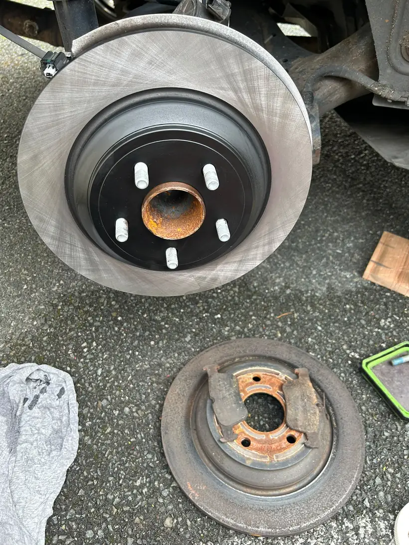 New brake disc fitted to the hub, the old rusted disc lying on the ground below it