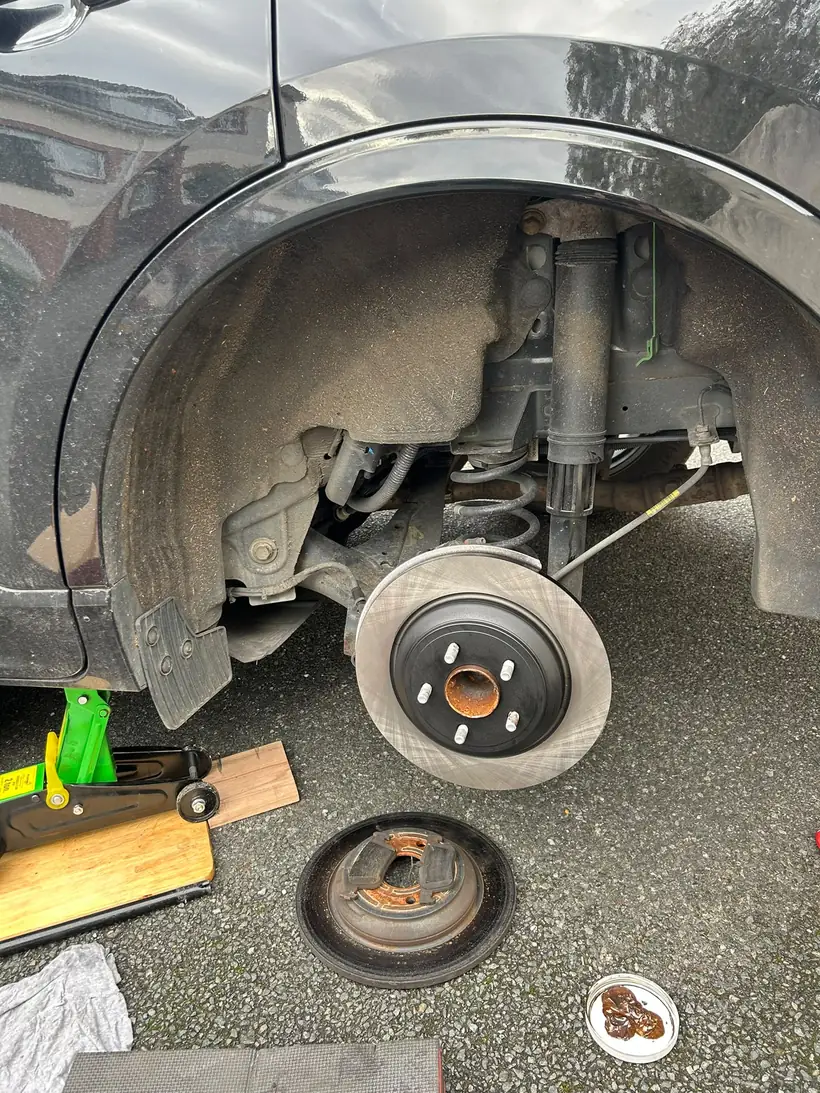 A mobile mechanic's brake job on a driveway, with the jack, the tools and the old disc on the ground
