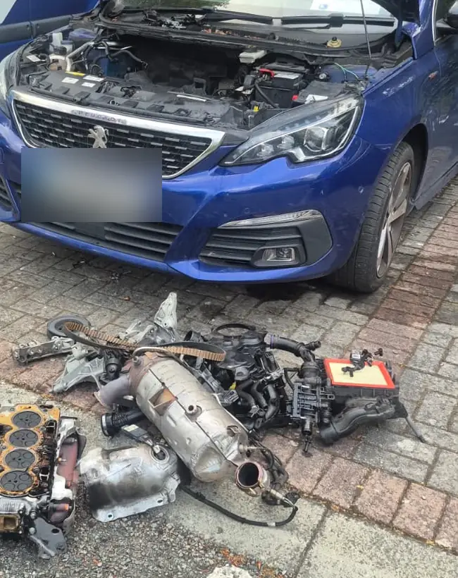 Hatchback with the bonnet open and engine parts laid out in front of it, repaired where it was parked
